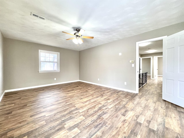 empty room with baseboards, visible vents, ceiling fan, wood finished floors, and a textured ceiling