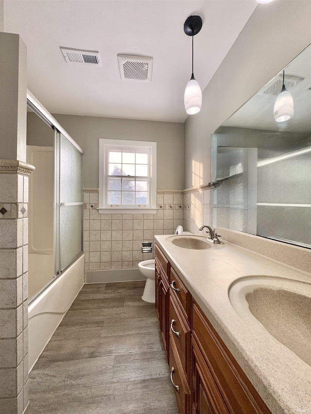 bathroom featuring visible vents, a sink, tile walls, and wood finished floors