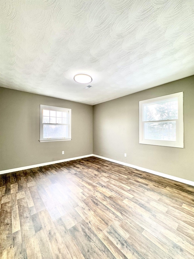 spare room with a textured ceiling, baseboards, and wood finished floors