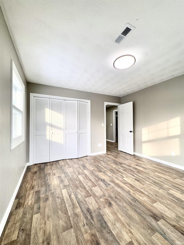 unfurnished bedroom with a closet, visible vents, baseboards, and wood finished floors