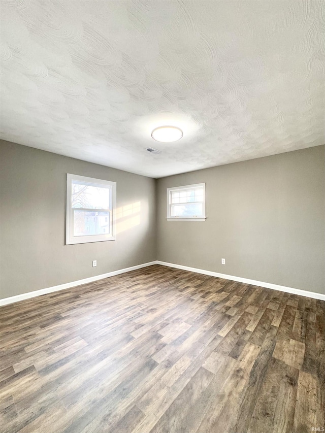 empty room with a textured ceiling, baseboards, and wood finished floors