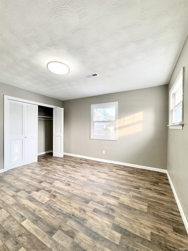 unfurnished bedroom featuring multiple windows, wood finished floors, and visible vents