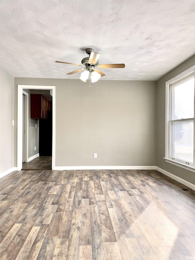 unfurnished room with a textured ceiling, wood finished floors, a ceiling fan, and baseboards