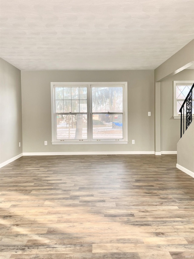 unfurnished room featuring a wealth of natural light, stairs, baseboards, and wood finished floors