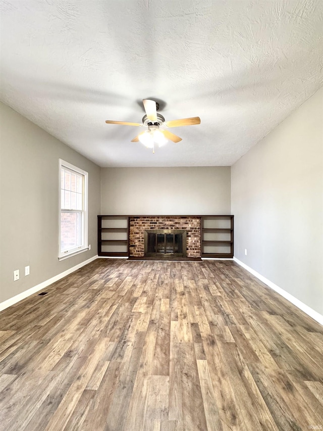 unfurnished living room featuring ceiling fan, a fireplace, wood finished floors, and baseboards