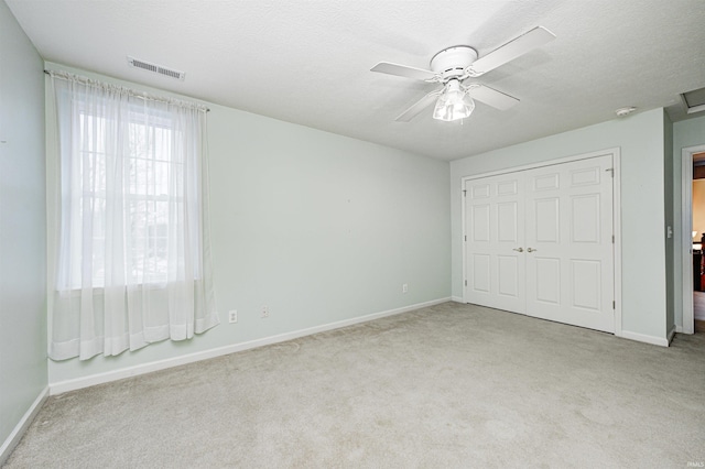 unfurnished bedroom with light colored carpet, a textured ceiling, ceiling fan, and a closet