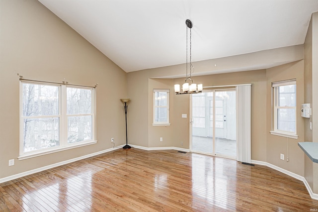 empty room featuring an inviting chandelier, lofted ceiling, and light wood-type flooring