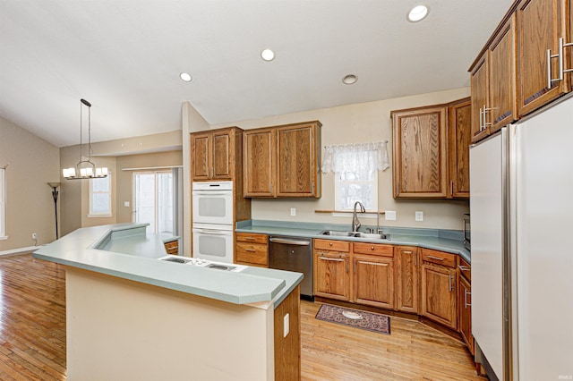 kitchen with decorative light fixtures, sink, light hardwood / wood-style floors, a center island with sink, and white appliances