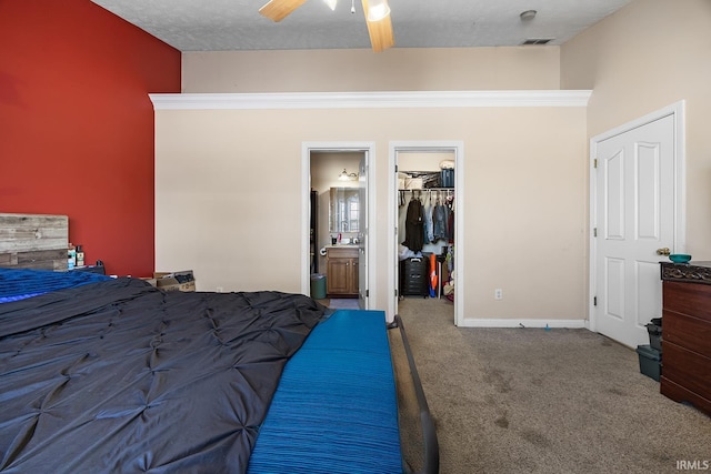 unfurnished bedroom with ensuite bath, carpet flooring, a walk in closet, ceiling fan, and a textured ceiling