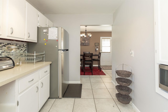 kitchen featuring light tile patterned flooring, stainless steel refrigerator, white cabinets, decorative backsplash, and hanging light fixtures