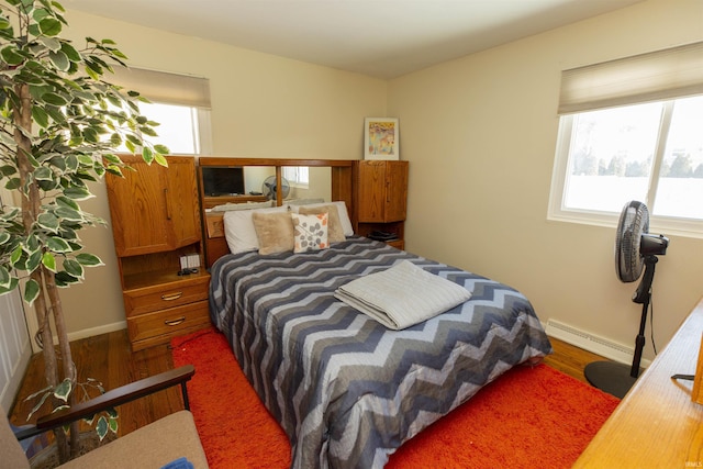 bedroom with hardwood / wood-style floors and a baseboard heating unit