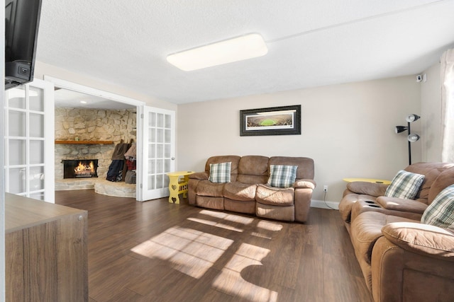 living room with a stone fireplace, dark hardwood / wood-style floors, a textured ceiling, and french doors