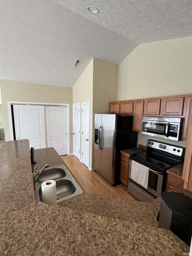 kitchen with sink, vaulted ceiling, light hardwood / wood-style flooring, a textured ceiling, and stainless steel appliances