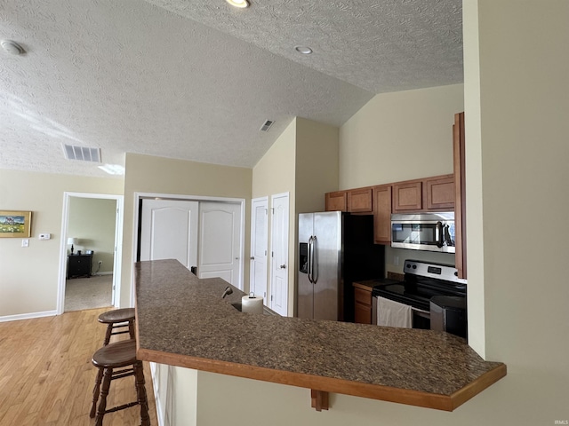 kitchen with lofted ceiling, a kitchen breakfast bar, kitchen peninsula, stainless steel appliances, and a textured ceiling