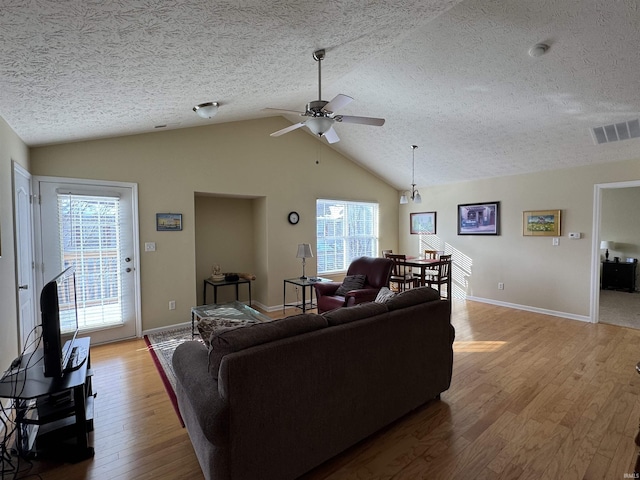 living room with ceiling fan, vaulted ceiling, a textured ceiling, and light hardwood / wood-style flooring