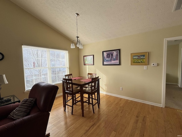 dining space featuring wood-type flooring, vaulted ceiling, a chandelier, and a textured ceiling