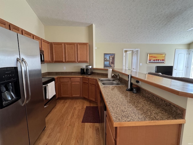 kitchen with sink, a textured ceiling, light hardwood / wood-style flooring, kitchen peninsula, and stainless steel appliances