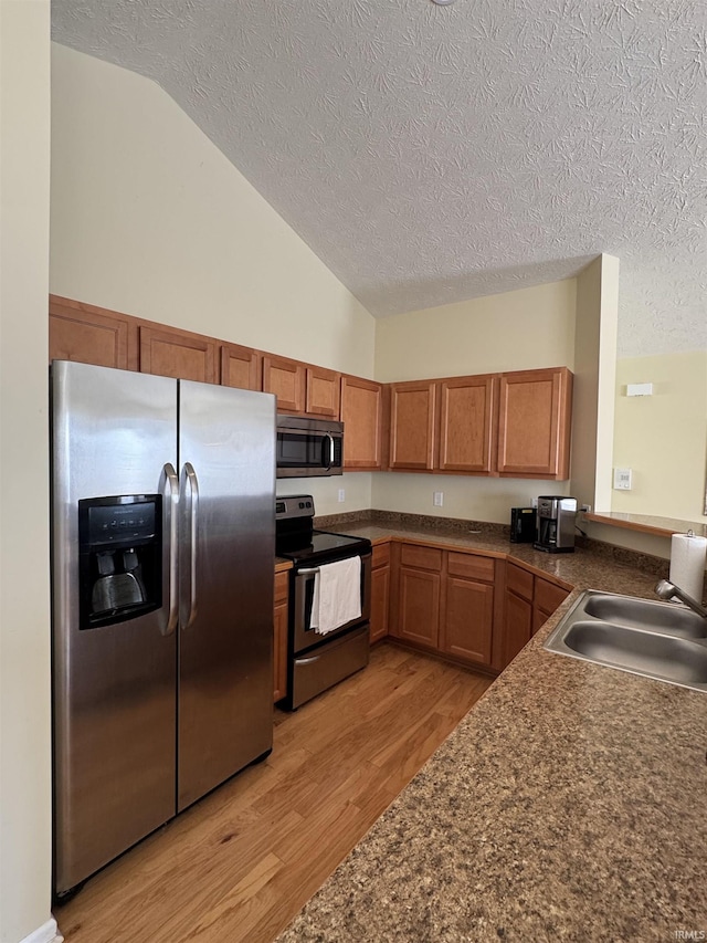 kitchen with stainless steel appliances, sink, a textured ceiling, and light hardwood / wood-style flooring