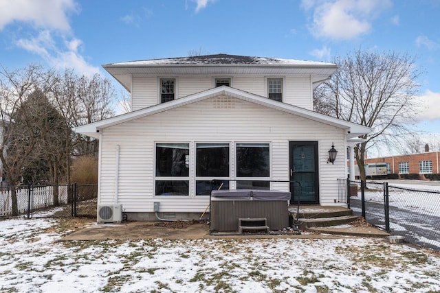 snow covered back of property with central AC, a hot tub, and ac unit