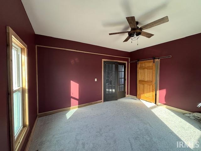 spare room with a barn door, ceiling fan, and carpet