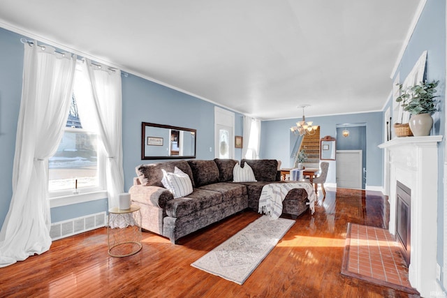 living area featuring a fireplace with flush hearth, wood finished floors, visible vents, ornamental molding, and an inviting chandelier