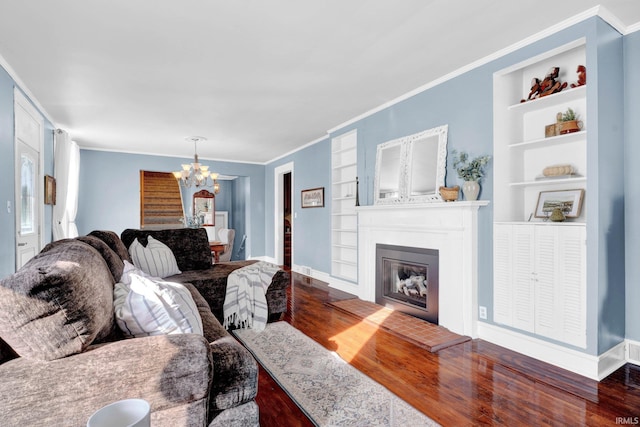 living room with built in features, a glass covered fireplace, a chandelier, and wood finished floors