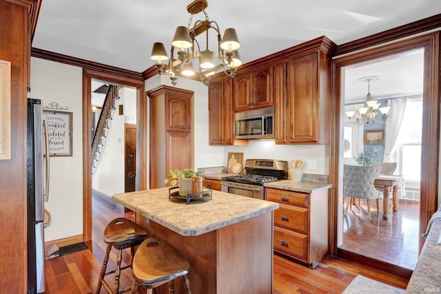 kitchen with a chandelier, hanging light fixtures, ornamental molding, stainless steel appliances, and light wood-type flooring