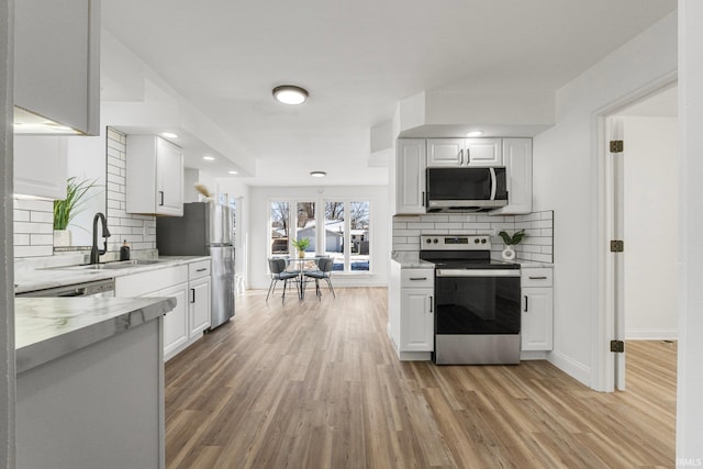 kitchen featuring light hardwood / wood-style flooring, white cabinetry, stainless steel appliances, light stone counters, and tasteful backsplash