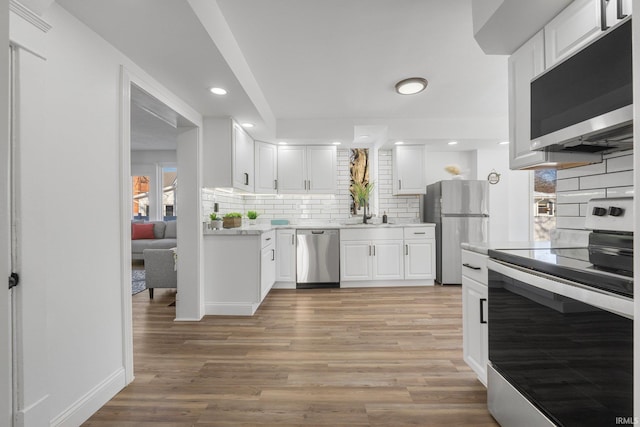 kitchen featuring sink, white cabinets, decorative backsplash, stainless steel appliances, and light wood-type flooring