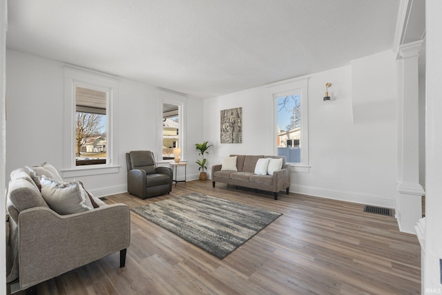 living room with ornate columns, wood-type flooring, a wealth of natural light, and a textured ceiling