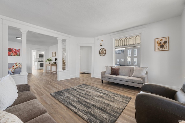 living room featuring decorative columns, light hardwood / wood-style flooring, and a textured ceiling