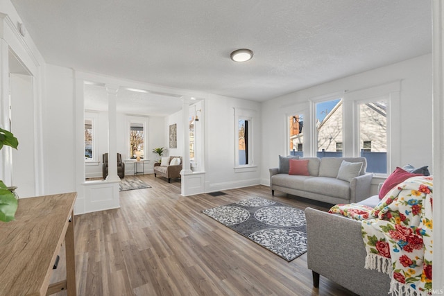 living room with decorative columns, a textured ceiling, and light hardwood / wood-style flooring