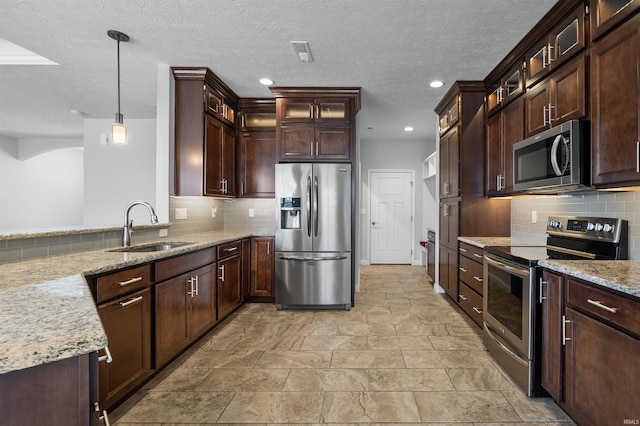 kitchen with appliances with stainless steel finishes, decorative light fixtures, light stone countertops, and sink