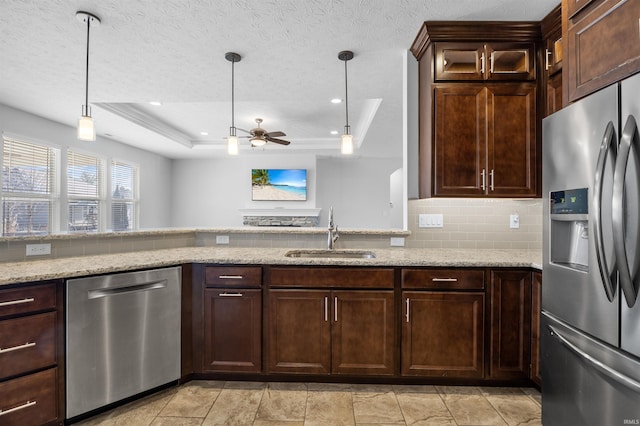 kitchen with appliances with stainless steel finishes, sink, hanging light fixtures, a tray ceiling, and light stone countertops