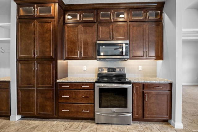 kitchen featuring stainless steel appliances, light stone countertops, dark brown cabinets, and decorative backsplash