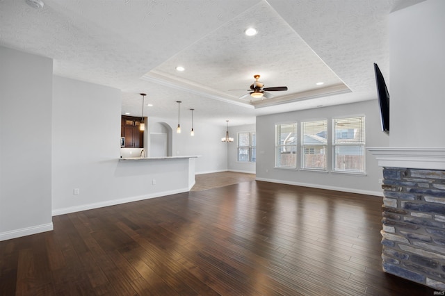 unfurnished living room featuring a raised ceiling, ceiling fan with notable chandelier, and a textured ceiling