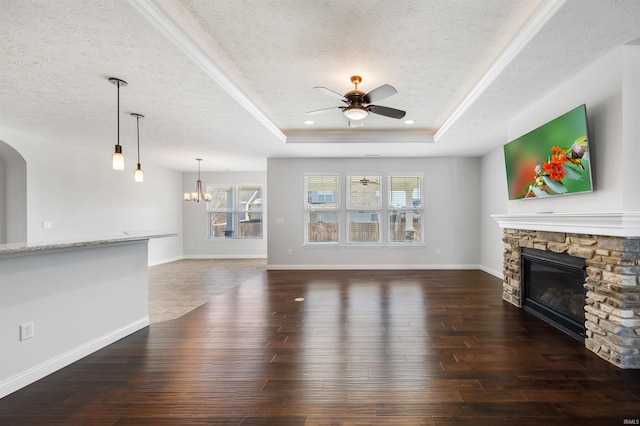 unfurnished living room featuring a tray ceiling, a stone fireplace, a textured ceiling, and ceiling fan with notable chandelier