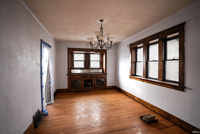 unfurnished dining area featuring an inviting chandelier, light hardwood / wood-style flooring, and a textured ceiling