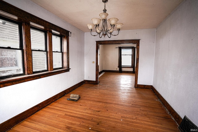 unfurnished dining area with hardwood / wood-style flooring, a notable chandelier, ornamental molding, and a wealth of natural light