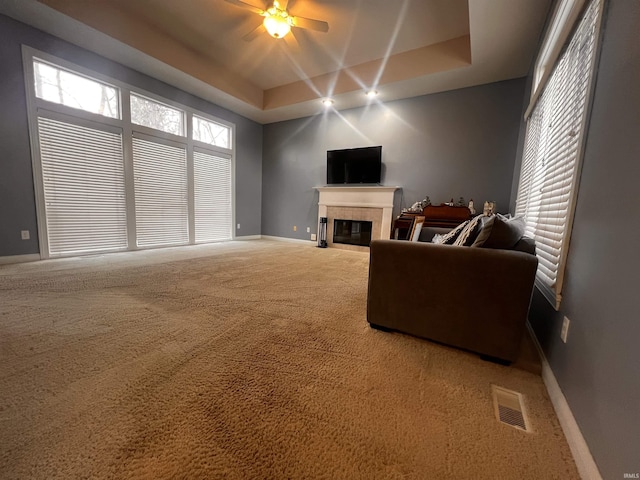 carpeted living room with a fireplace, a raised ceiling, and ceiling fan