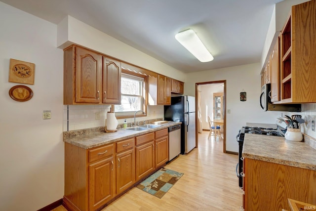 kitchen with appliances with stainless steel finishes, sink, backsplash, and light hardwood / wood-style floors