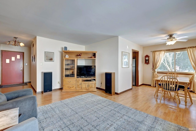 living room featuring ceiling fan with notable chandelier and light hardwood / wood-style flooring