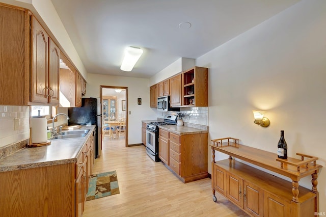 kitchen featuring appliances with stainless steel finishes, sink, light wood-type flooring, and backsplash