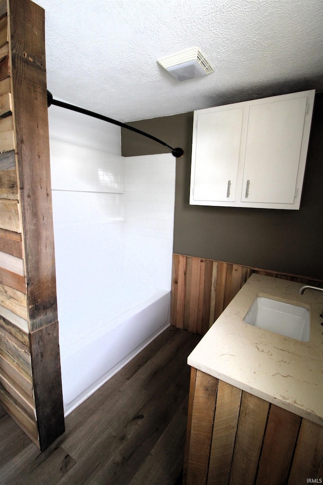 washroom featuring sink, wooden walls, dark hardwood / wood-style floors, and a textured ceiling