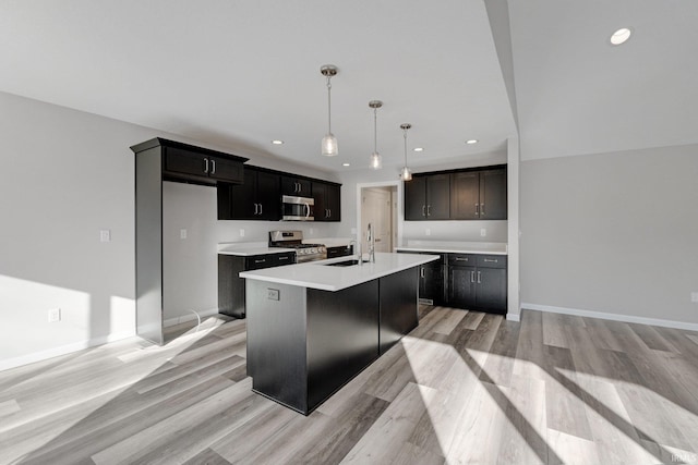 kitchen featuring decorative light fixtures, an island with sink, sink, light hardwood / wood-style floors, and stainless steel appliances