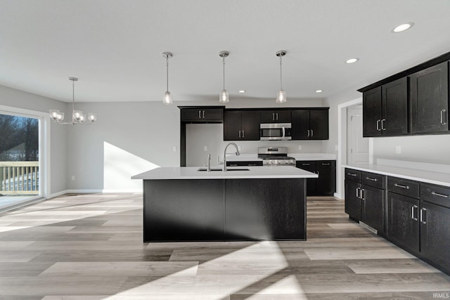 kitchen featuring pendant lighting, sink, a kitchen island with sink, light hardwood / wood-style floors, and stainless steel appliances