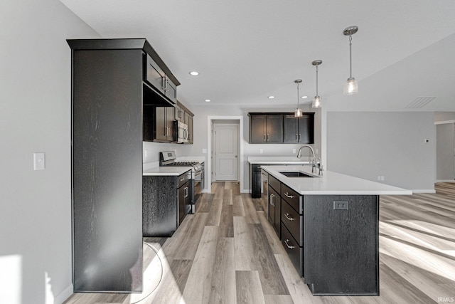 kitchen with appliances with stainless steel finishes, an island with sink, sink, hanging light fixtures, and dark brown cabinetry