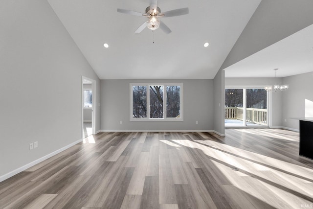 unfurnished living room featuring high vaulted ceiling, a healthy amount of sunlight, ceiling fan with notable chandelier, and light wood-type flooring