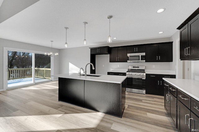 kitchen with decorative light fixtures, sink, stainless steel appliances, a center island with sink, and light wood-type flooring