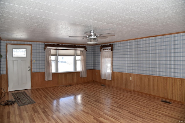 interior space featuring crown molding, ceiling fan, light wood-type flooring, and wood walls